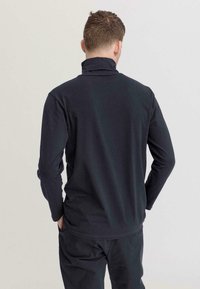 Dunkelgraues langärmliges Hemd mit hohem Kragen, das eine weiche Textur und einen lockeren Schnitt aufweist. Die Rückseite zeigt ein einfaches Design ohne Muster.