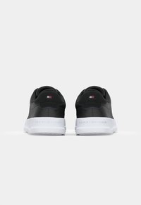 Czarne trampki z gładką skórzaną cholewką, białą gumową podeszwą i wytłoczonym logo na pięcie. Zawierają mały kolorowy detal w formie flagi.