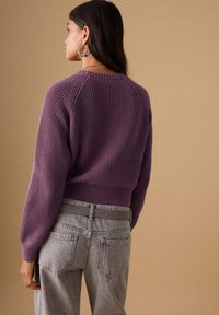 Pull tricoté violet à texture côtelée, avec manches longues et ourlet court, associé à un jean taille haute gris clair.