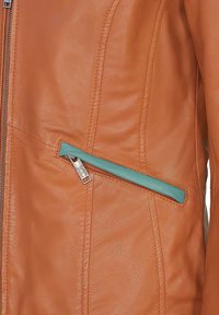 Orange läderjacka med en dragkedjeficka med teal-accent, slät textur och söm detaljer längs sömmarna.