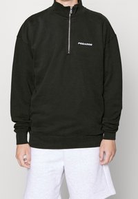 Černá mikina s půlzipem vyrobená z bavlny, s vysokým límcem, žebrovanými manžetami a bílým logem "PEGADOR" na hrudi.