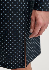 Schwarzes Baumwollhemd mit einem geometrischen Diamantmuster in Blau und Hellblau, mit einem seitlichen Schlitz und einem dezenten Markentag.