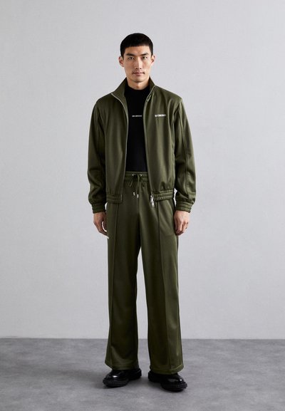 Λαδί tracksuit που αποτελείται από τζάκετ με φερμουάρ και παντελόνι με κορδόνι, φτιαγμένο από μαλακό ύφασμα, με άνετη εφαρμογή και διακριτική σήμανση.