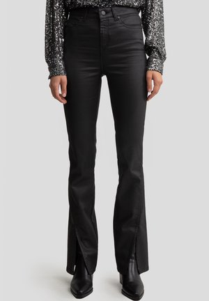 Nainen, joka pukeutunut korkeavyötäröisiin mustiin nahkahousuihin, joissa on etureikät lahkeiden helmassa, yhdistettynä mustiin teräväkärkisiin saappaisiin ja hopeiseen paljettimekkoon.