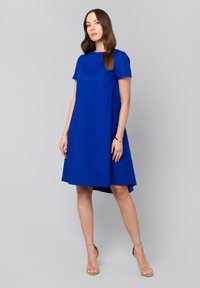 Sukienka o krótkim rękawie, do kolan, w intensywnym niebieskim kolorze, z okrągłym dekoltem i asymetrycznym dołem. Gładki materiał o delikatnym połysku.