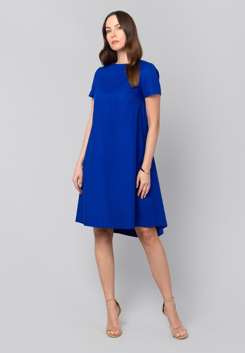 Sukienka o krótkim rękawie, do kolan, w intensywnym niebieskim kolorze, z okrągłym dekoltem i asymetrycznym dołem. Gładki materiał o delikatnym połysku.