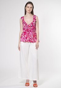Lyserød blomster peplum top med flæser, der har en dyb V-udskæring og en tætsiddende talje. Båret med hvide bukser med bred ben og orange hæle sandaler.
