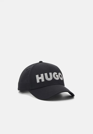 Casquette de baseball noire à visière courbée avec de grandes lettres blanches texturées formant "HUGO" sur le panneau avant.