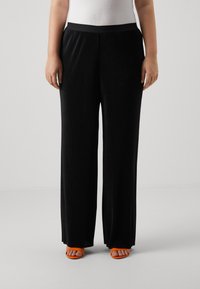 Black wide-leg trousers with vertical ribbed texture, elastic waistband, and orange open-toe sandals. Smooth fabric, relaxed fit.