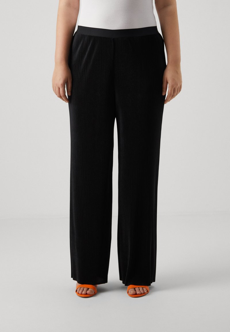 Black wide-leg trousers with vertical ribbed texture, elastic waistband, and orange open-toe sandals. Smooth fabric, relaxed fit.