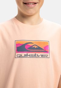 Persikofärgad bomull t-shirt med en flerfärgad grafisk design som visar vågor och berg, samt texten "Quiksilver" i svart.