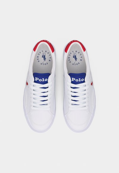 Λευκά sneakers Polo Ralph Lauren με κόκκινα στοιχεία στην φτέρνα, μπλε ετικέτες στη γλώσσα, δεμένα κορδόνια και το λογότυπο με το άλογο στο πλάι, φωτογραφημένα από ψηλά σε λευκό φόντο.