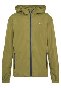 Olive green jacket o lekkiej wadze z kapturem, pełnym zamkiem błyskawicznym z przodu oraz granatowymi akcentami. Posiada elastyczne mankiety i mały detal logo.