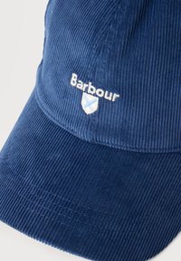 Μπλε καπέλο μπεϊζμπόλ από κοτλέ με το λογότυπο "Barbour" και έμβλημα ασπίδας κεντημένα σε λευκό και ανοιχτό μπλε στην μπροστινή πλευρά.