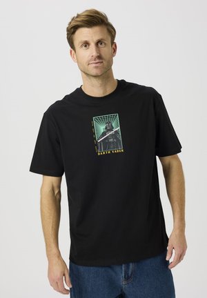 Camiseta negra de algodón con estampado gráfico de Darth Vader en verde y amarillo. Corte holgado con mangas cortas y cuello redondo.