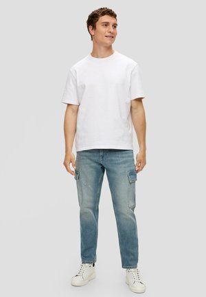 T-shirt en coton blanc, à manches courtes, col rond. Jean cargo bleu clair avec des détails de poches. Baskets blanches avec des accents noirs.
