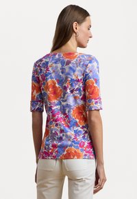 Haut à manches courtes à motifs floraux dans des teintes de violet, d'orange et de rose ; texture lisse avec un col rond et des poignets roulés.
