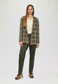 Dubbelgevouwen blazer van groen geruit stof, gecombineerd met olijfgroene broek en bruine sneakers. Minimalistische witte top eronder.