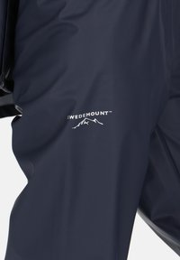 Marineblauer Regenmantel aus wasserdichtem Material mit glatter Oberfläche. Auf der Vorderseite befindet sich ein weißes "SWEDEMOUNT"-Logo und ein Bergmotiv.