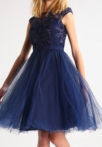 Námořnické modré šaty s krátkými rukávky, krajkovým korpusem a tylovou sukní. Obsahují květinovou výšivku a přiléhavý pas.