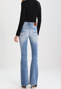 Ljusblå utsvängda denimjeans med blekning, kontrasterande sömmar och en brun läderlapp på bakre midjebandet.