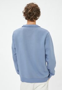 Felpa blu, tessuto morbido, vestibilità ampia, collo e polsini a coste, design minimalista, senza motivi o loghi visibili, vista posteriore semplice.