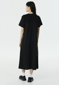 Zwarte maxi jurk met korte mouwen, getextureerd bovenstuk en meerkleurige zijpaneel. Gepaard met zwarte sneakers en witte sokken.