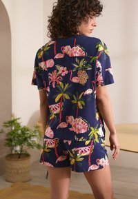 Ensemble de pyjama bleu marine à manches courtes et shorts, présentant un imprimé tropical vif avec des flamants roses, des ananas et des fleurs en rose et vert.