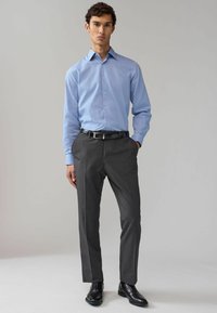 Camicia azzurro chiaro con un motivo sottile, abbinata a pantaloni grigi scuri e scarpe nere. Fit pulito e su misura, aspetto lucido.