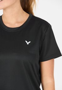 Sort atletisk t-shirt med rund halsudskæring, korte ærmer og en glat tekstur. Har et lille hvidt logo på venstre bryst.