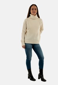 Maglione a coste color crema con colletto alto, abbinato a jeans skinny blu e stivaletti neri con tacco.