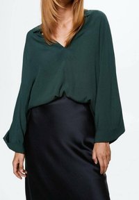 Blouse légère vert foncé avec un décolleté en V et des manches amples, associée à une jupe en satin noir à la texture douce.