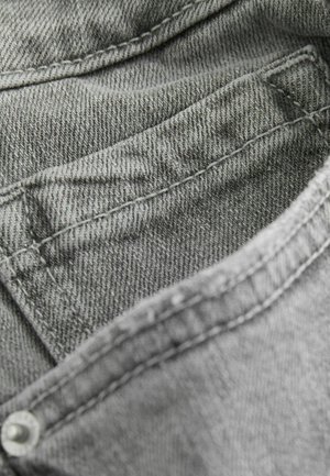 Grå denimtyg med en texturerad yta, med synliga sömmar längs kanterna och en liten ficka. Tyget är mjukt och böjbart.