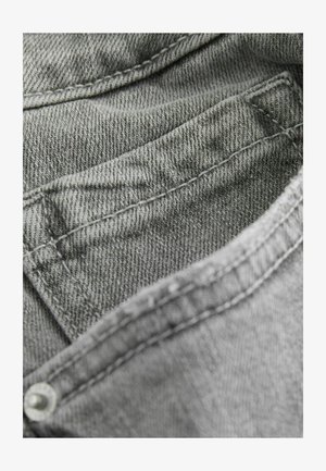 Grå denimtyg med en texturerad yta, med synliga sömmar längs kanterna och en liten ficka. Tyget är mjukt och böjbart.