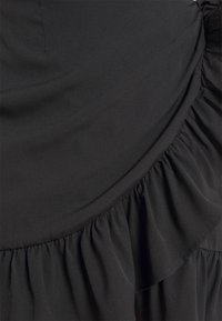 Tissu de robe noire présentant une surface lisse, des volants plissés le long de l'ourlet et des détails de drapé subtils. Aucun accessoire visible.