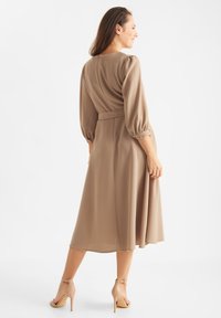 Knee-length, béžové šaty s dlhými, nariasenými rukávmi, priliehavým pásom a splývavou sukňou. Hladká látka s jemným leskom. V kombinácii s béžovými podpätkami.