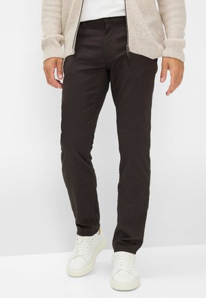 Dark brown cotton pants with a fitted design, paired with white sneakers. Texture appears smooth with a subtle weave pattern.