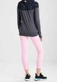 Marinblå hoodie med mönstrad yoke, grå kropp, rosa smala byxor och svarta sneakers med akvamarinfärgade detaljer, med sidoflikar.