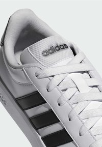 Hvid Adidas-sneaker med sorte striber, hvide snørebånd og Adidas-logo på polstret tunge, vist fra top-sides vinkel.