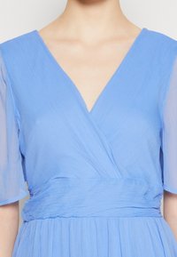 Robe bleu clair avec un col en V, un design portefeuille et des manches courtes et transparentes. Tissu texturé avec une taille ajustée et une jupe fluide.