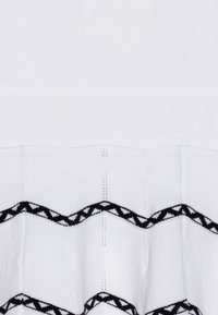 Biely textil s textúrovaným povrchom obsahuje čiernobandá s cik-cak vzorom a trojuholníkovými akcentmi pod dolným okrajom.