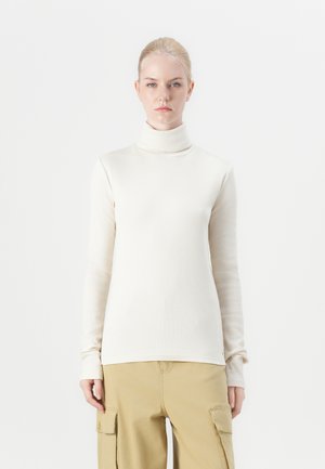 Long-sleeve turtleneck sweater in light cream, ribbed texture, soft fabric, fitted design, paired with khaki cargo pants.