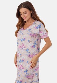 Kwiatowa koszula nocna w miękkim beżowym materiale, z fioletowymi i niebieskimi wzorami kwiatów, krótkimi rękawami oraz dekoltem w kształcie litery V.
