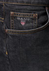 Černé džínové kalhoty s žlutým prošitím. Mají malou zadní kapsu s výšivkou loga GANT, kovové knoflíky a texturovanou tkaninu.