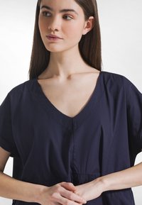 Marineblaues Kleidungsstück mit V-Ausschnitt und kurzen Ärmeln. Hergestellt aus glattem Stoff, mit einer gerafften Taille und dezenten Nahtdetails.