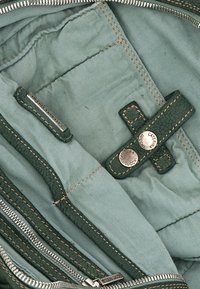 Interno in tessuto verde con una texture liscia, caratterizzato da scomparti con zip e bottoni. Include etichette del marchio e dettagli di cuciture a contrasto.