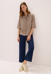 Beige kortärmad skjorta med knappar, kombinerad med vida blå jeans och ljusa sneakers. Slät tyg och skräddarsydd passform.