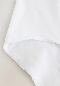 Weißes Baumwollkleidungsstück mit einer geschwungenen Spitzenborte am Saum, das eine weiche Textur und ein einfaches, klares Design aufweist.