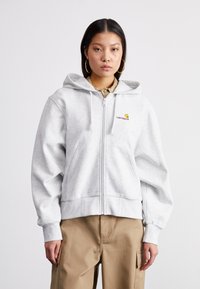 Grå zip-up hettegenser med en tilpasset midje, stor hette og frontlommer. Carhartt-logoen er brodert i gult og mørkerødt.