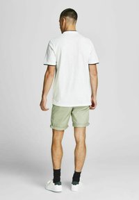 Wit poloshirt met zwarte accenten, lichtgroene shorts en witte schoenen. Zichtbare naden en opgerolde shorts. Eenvoudig ontwerp, geen patronen.